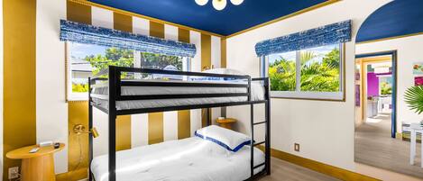 A bunk bed room with a ceiling fan, a small round table, and a window with a view of greenery.