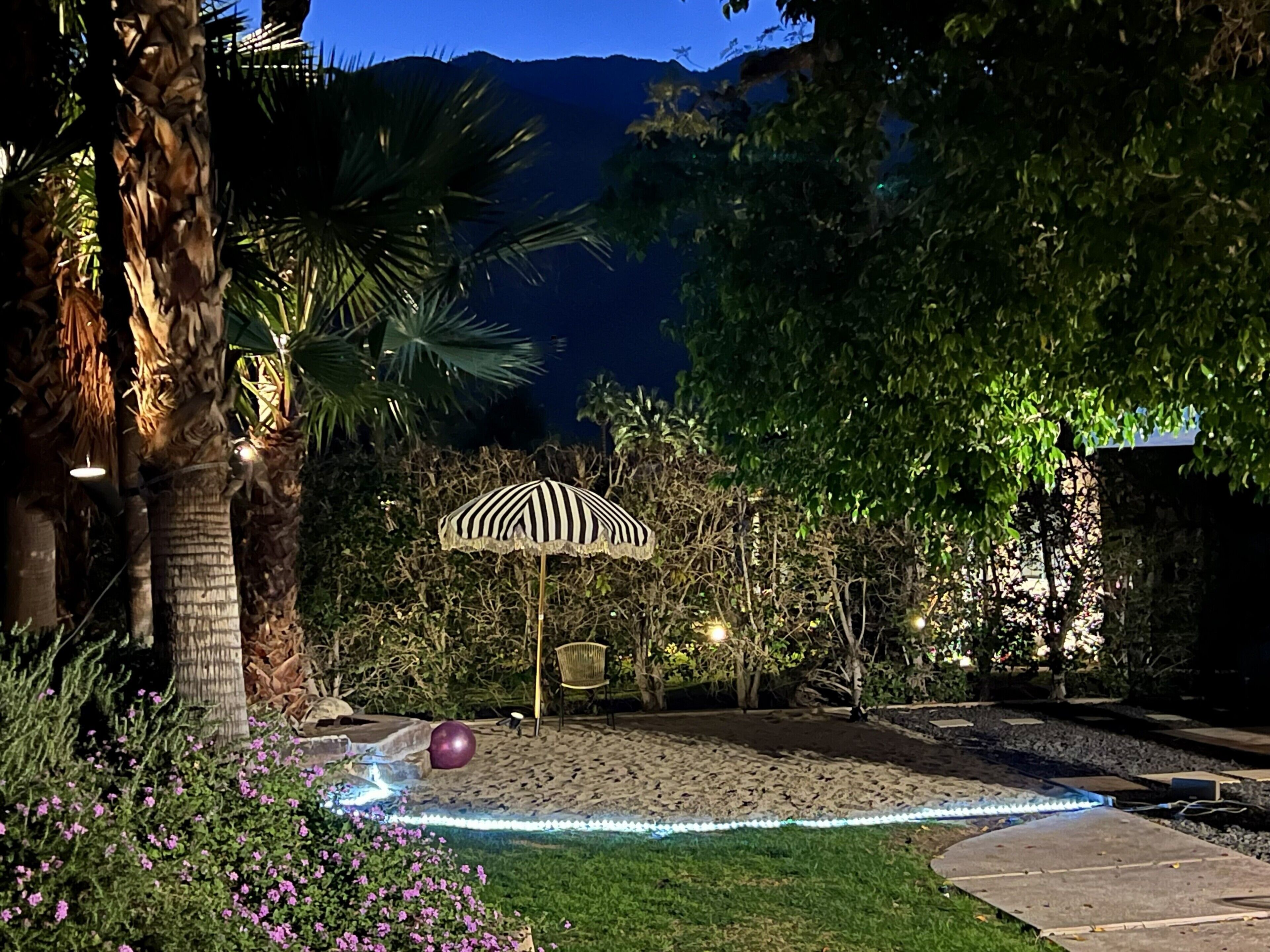 A nighttime outdoor area with a patterned umbrella, a stone bench, and a pathway.