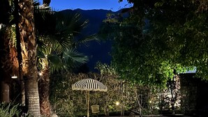 A nighttime outdoor area with a patterned umbrella, a stone bench, and a pathway. - Stylish Chic Escape, Private Pool & Golf Course Residence. Fun & Fabulousity (Palm Springs)