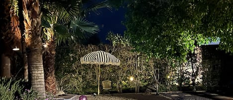 A nighttime outdoor area with a patterned umbrella, a stone bench, and a pathway.