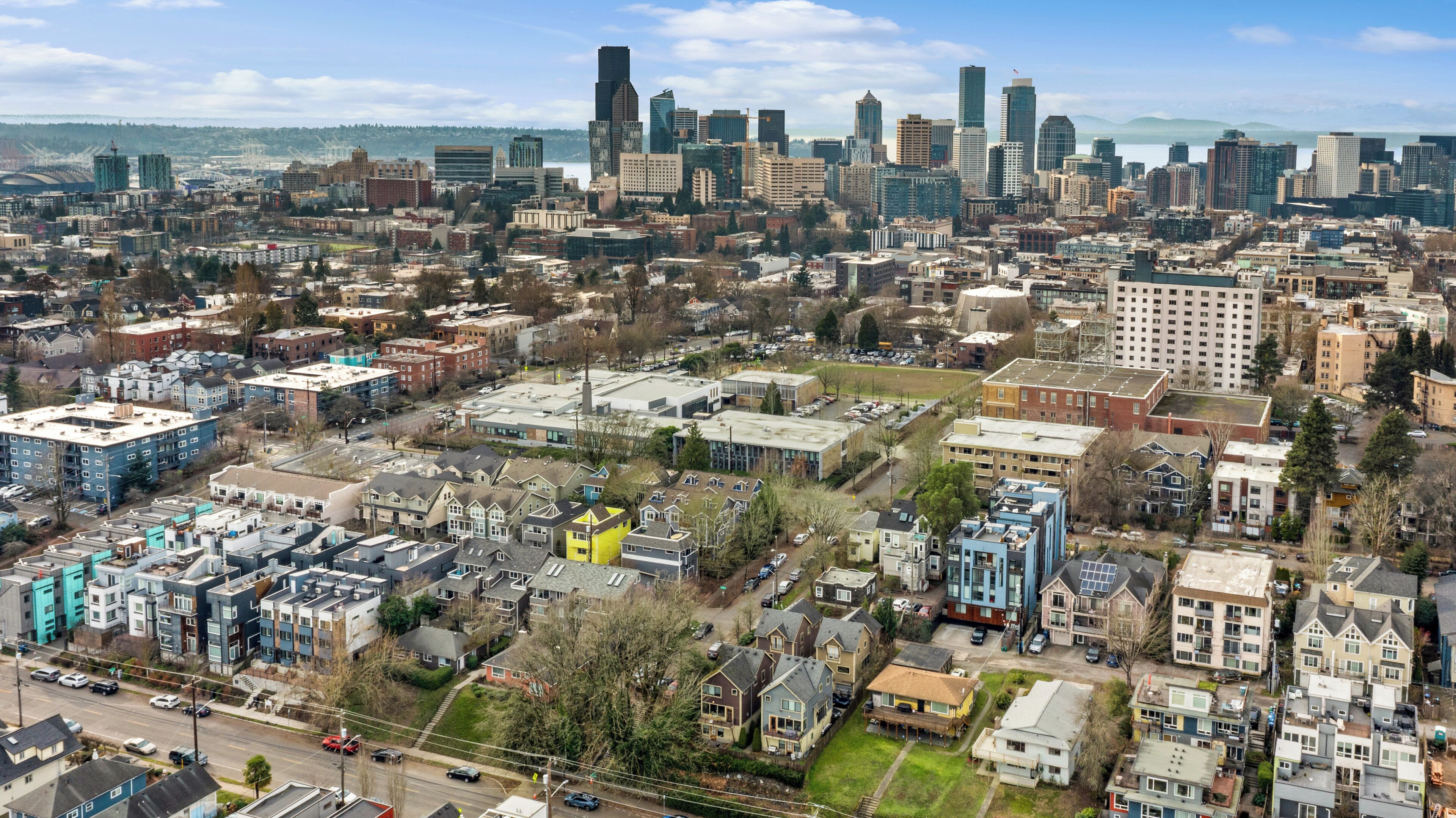 A cityscape with a mix of residential and commercial buildings, including high-rise office buildings and a variety of housing styles.