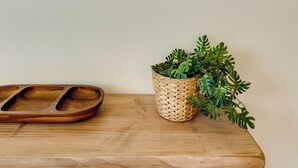 Drie ingelijste kunstwerken aan een muur, een houten dienblad en een gevlochten mand met groene planten.