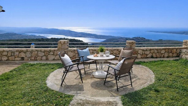 Un patio con mesa y sillas que da a una vista panorámica del agua y las colinas.