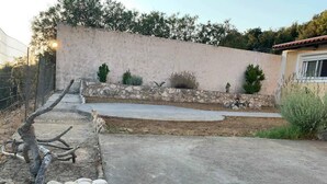 Un camino pavimentado que conduce a una casa con un muro de piedra y un pequeño jardín con arbustos y un cactus.