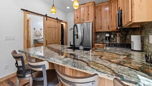 Una cocina con armarios de madera, encimera de granito, electrodomésticos de acero inoxidable e iluminación colgante.