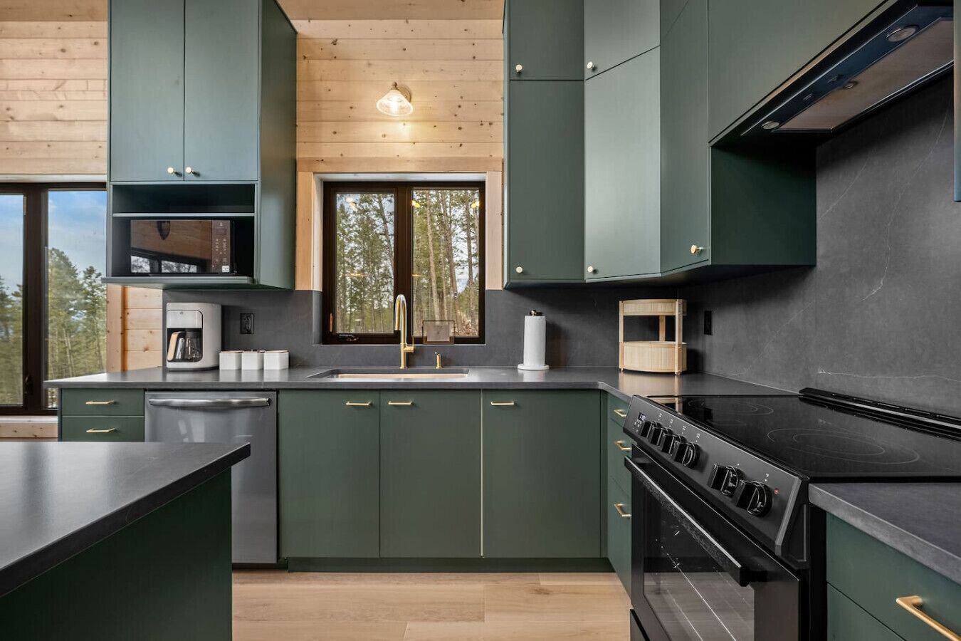 Una cocina moderna con armarios verde oscuro, encimera negra y estufa empotrada.