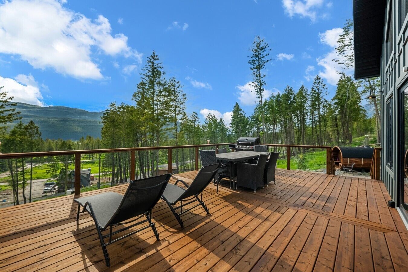 En træterrasse med udendørs møbler, grill og udsigt til skov og bjerge.