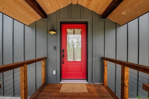 A red door with a glass panel, a wooden handrail, a light fixture, and a wooden ceiling.