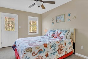 A bedroom with a bed, a ceiling fan, two windows, and wall decorations.