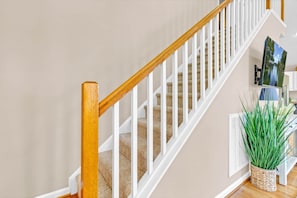 A staircase with white railings and wooden handrails, carpeted steps, and a potted plant on the landing.