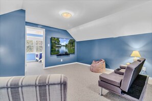 A living room with a flat-screen TV mounted on the wall, a sofa, a bean bag, and a lamp.