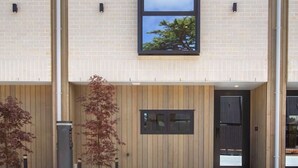 Un edificio moderno con un gran ventanal, una puerta de madera y un pequeño jardín con plantas.