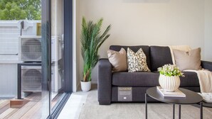 Una sala de estar moderna con un sofá gris, una planta en maceta y una mesita con un libro y flores.