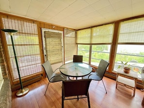 A room with a round glass table, four chairs, a floor lamp, and large windows with blinds.