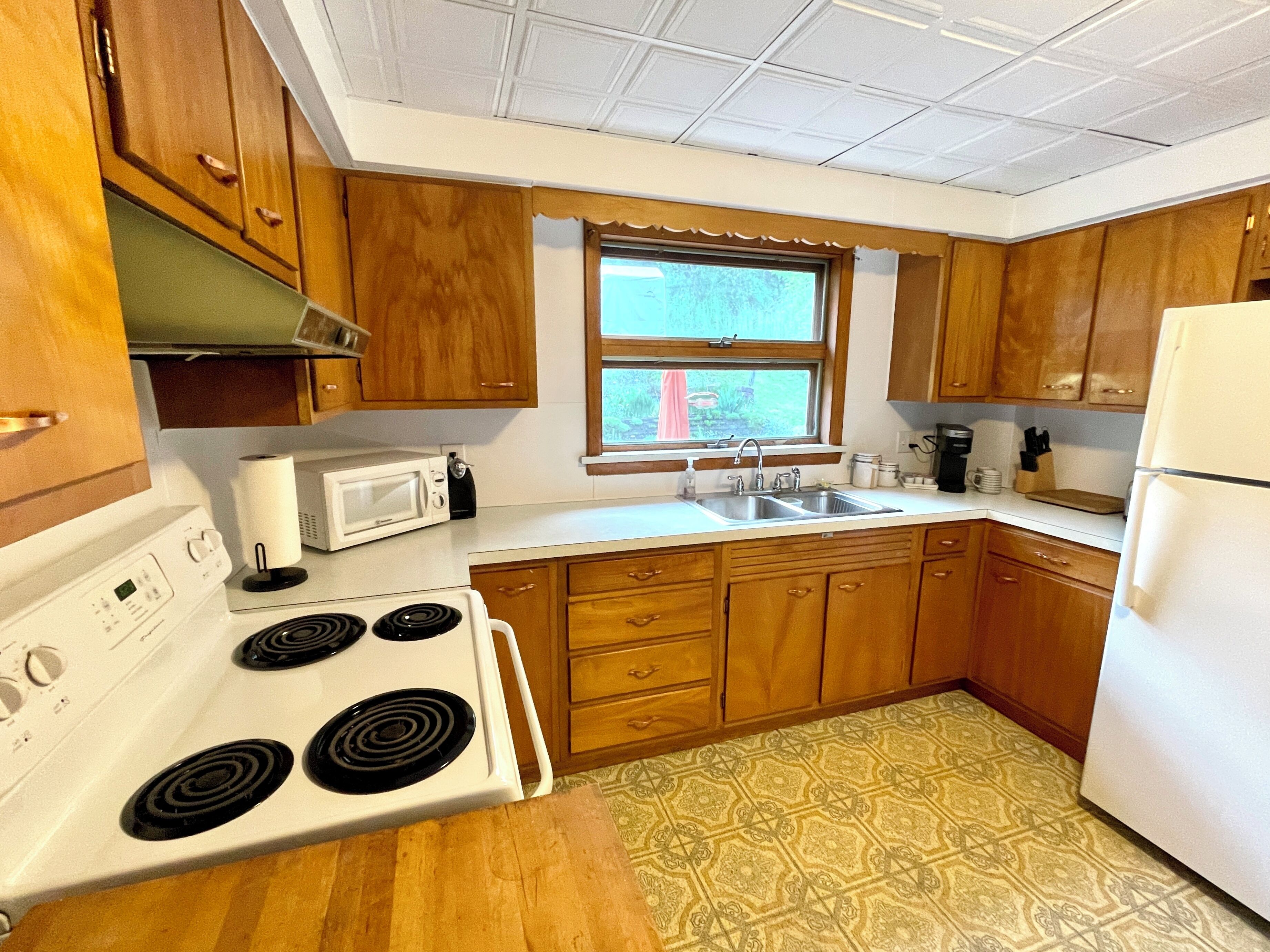 A kitchen with wooden cabinets, a white stove, a microwave, and a window.