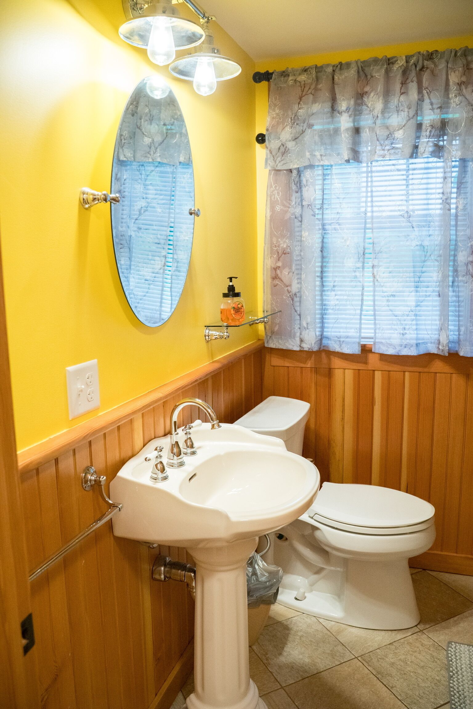 A bathroom with a white sink, a toilet, a mirror, and a window with curtains.