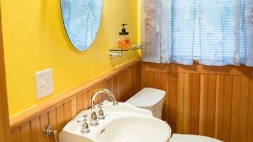 A bathroom with a white sink, a toilet, a mirror, and a window with curtains.