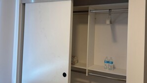 Una habitación con un armario blanco, un perchero con un cepillo de dientes y una botella de agua en la estantería.