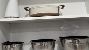Una estantería blanca con un jarrón blanco, un recipiente metálico y tres cuencos metálicos.