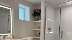 Un baño moderno con ducha de vidrio, un espejo grande y un inodoro.