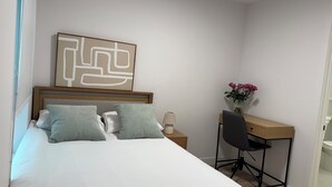 Un dormitorio con una cama, un escritorio, una silla, una lámpara y un florero con flores.
