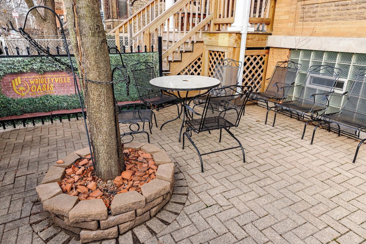 An outdoor patio area with a round table and chairs, a tree, and a brick fire pit.