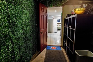 A hallway with a green wall, a red door, and a blue mat leading to a room.