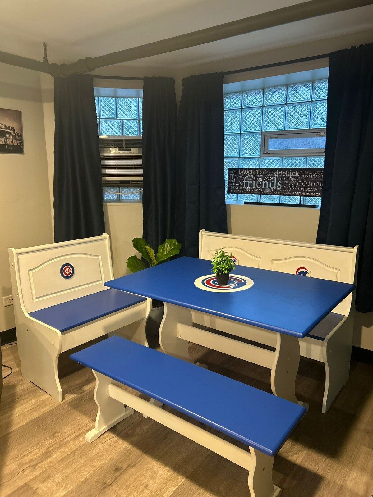 A room with a table and benches, a potted plant, and a window with curtains.