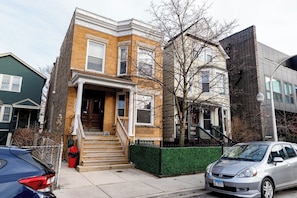 A two-story residential building with a front entrance, a small porch, and a staircase leading to the entrance.