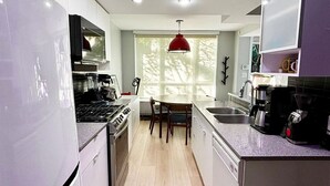 A modern kitchen with white cabinets, a stove, and a dining area with a red pendant light. - Cozy 2-bedroom townhome in beautiful Vancouver with AC (Vancouver)