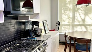 A modern kitchen with a gas stove, oven, and microwave. There is a dining table with chairs and a red pendant light. - Cozy 2-bedroom townhome in beautiful Vancouver with AC (Vancouver)