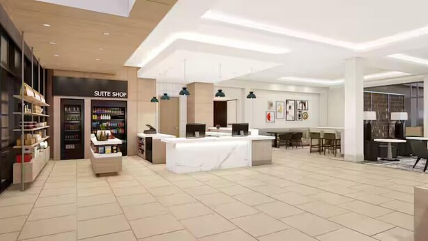 Un lobby moderno de hotel con mostrador de recepción, un letrero que dice 'SUITE SHOP' y un área de descanso con mesas y sillas.