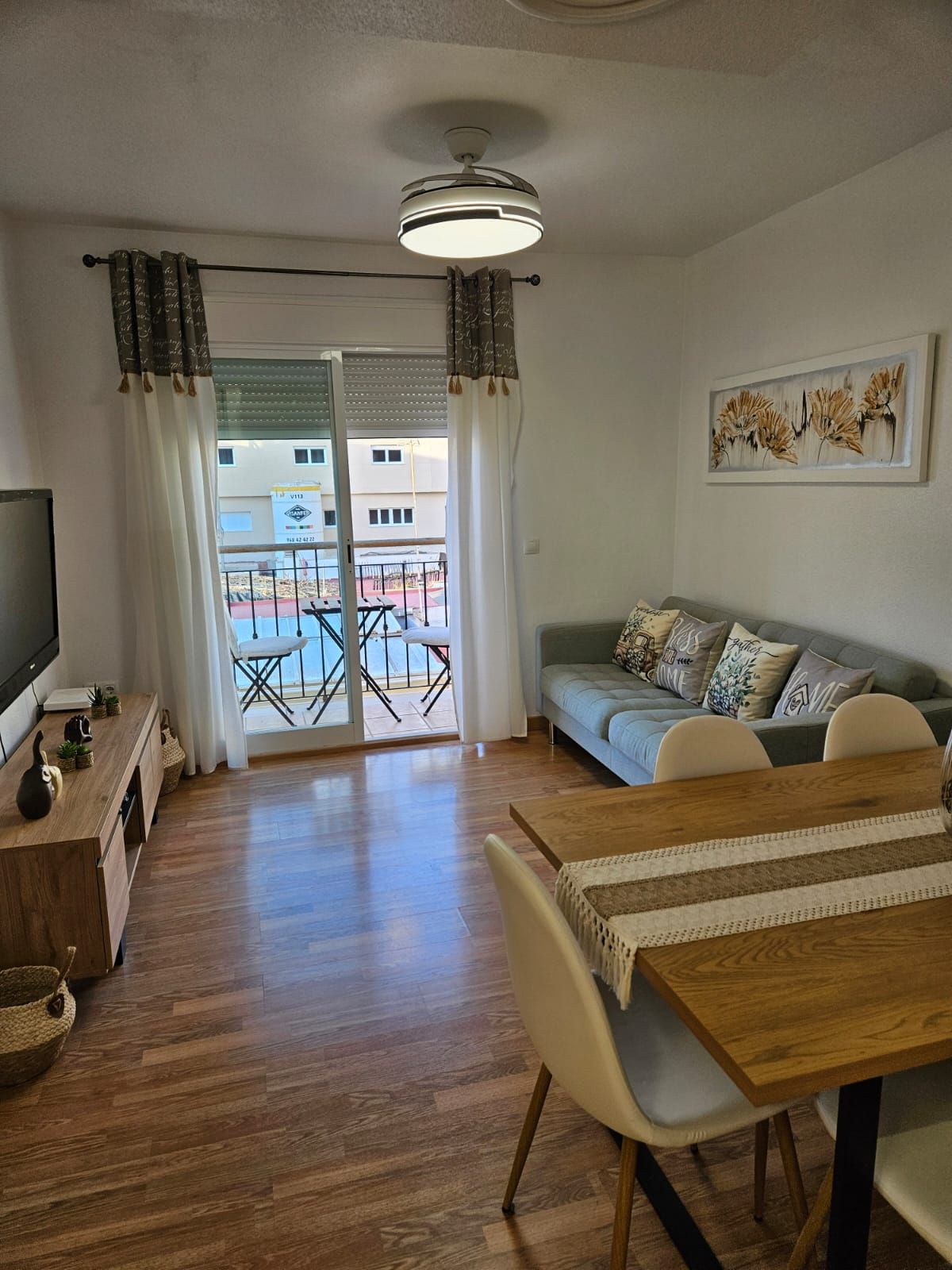 Un salon comprenant un canapé, une table à manger, un téléviseur et un balcon offrant une vue sur les immeubles.