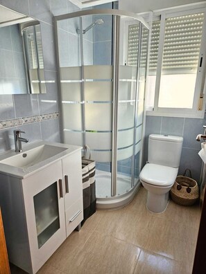 Un baño moderno con ducha envuelta en vidrio, lavamanos, inodoro y espejo.