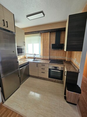 A modern kitchen with stainless steel appliances, wooden cabinets, and a tiled backsplash.