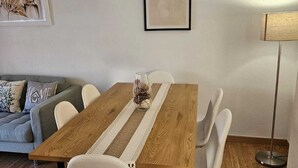 Ruokailutilassa on puinen pöytä, valkoiset tuolit, sohva ja seinällä oleva kehystetty taideteos.