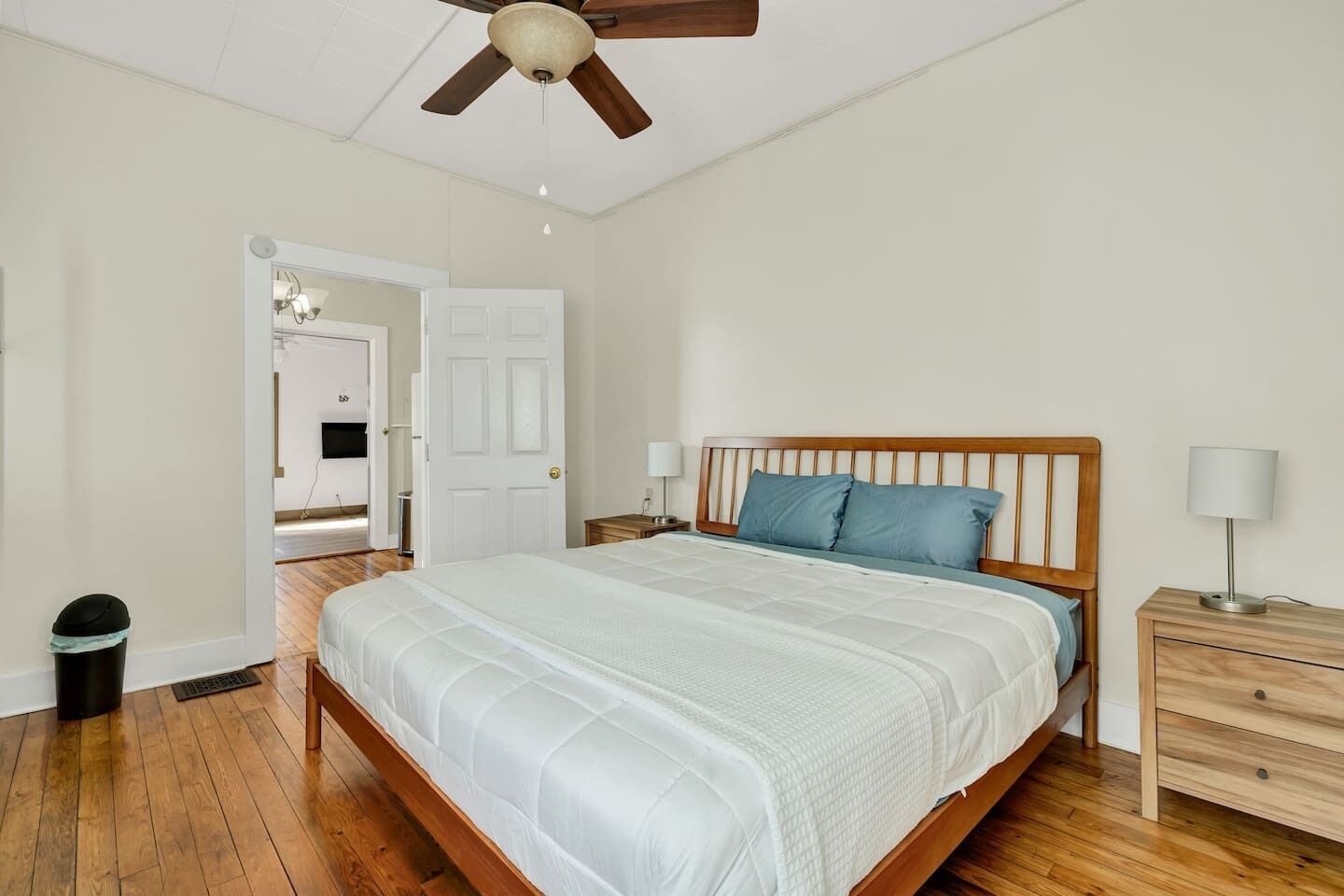 A bedroom with a wooden bed, a nightstand, a lamp, and a ceiling fan.