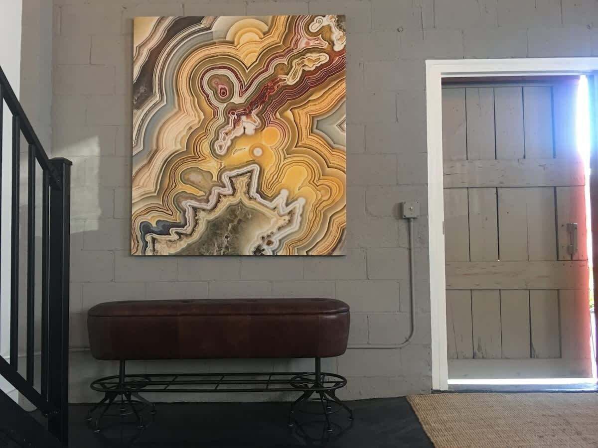 Um quarto com uma obra de arte na parede com padrão de mármore, um banco marrom e uma porta de madeira.