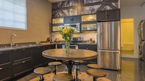 Une cuisine moderne dotée d’un îlot central, d’appareils électroménagers en acier inoxydable et de meubles de rangement aux couleurs sombres.