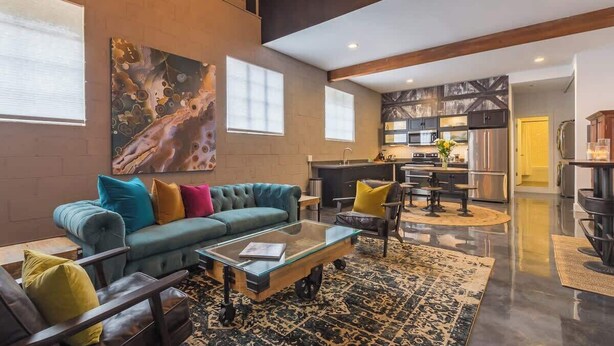 Un vaste espace de vie agrémenté d’un canapé moderne, d’une table basse en verre et d’un grand tableau abstrait accroché au mur.