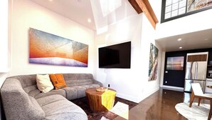 A modern living room with a grey sectional sofa, a wooden coffee table, and a flat-screen TV mounted on the wall.