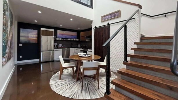 A modern kitchen with a dining area, a staircase, and a view of the city.