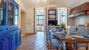 Un comedor con una mesa de madera, sillas estampadas en azul, un armario azul y vistas a través de un ventanal abierto.