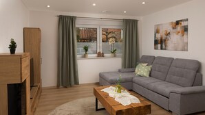 Un salón moderno con un sofá gris, una mesa de centro de madera y un ventanal con cortinas.