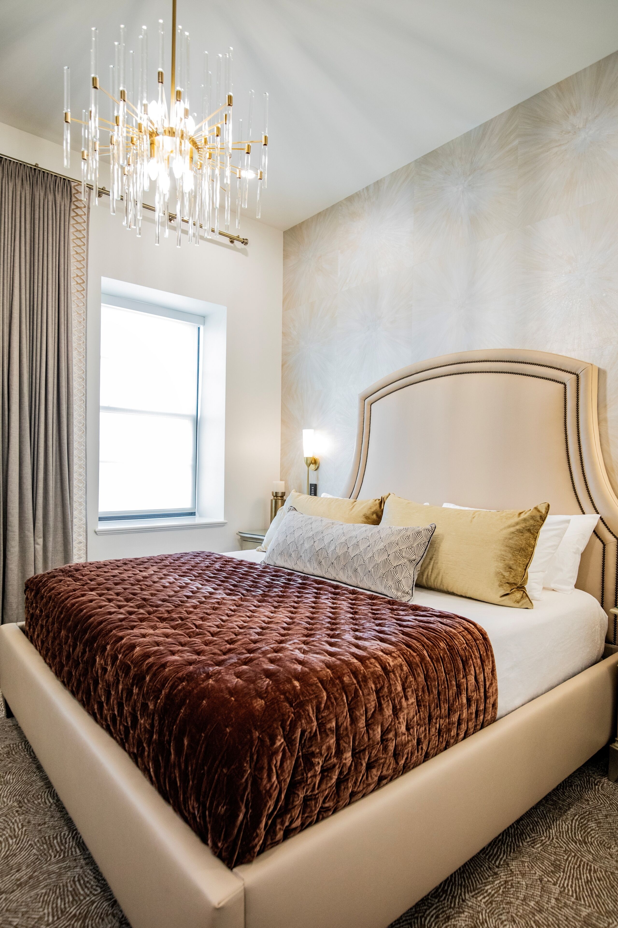 A bedroom with a large bed, a chandelier, a window, and a nightstand.
