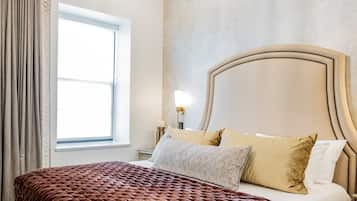 A bedroom with a large bed, a chandelier, a window, and a nightstand.