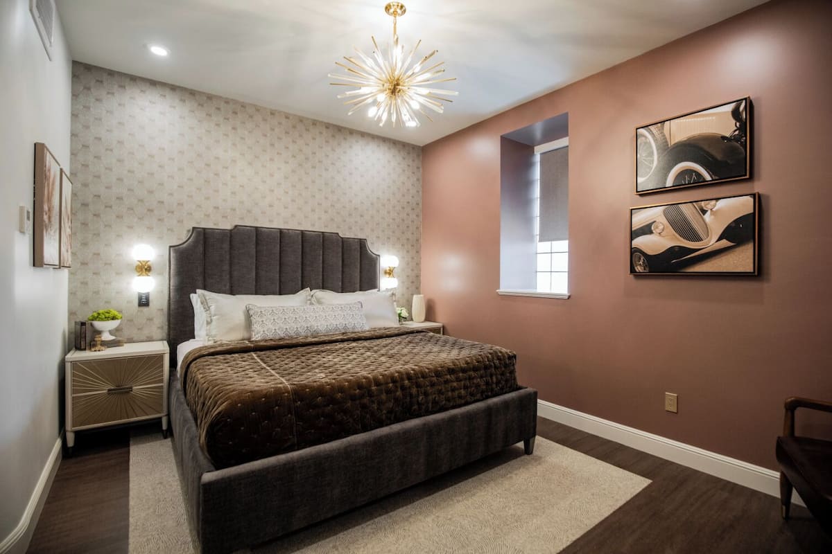 A bedroom with a large bed, a nightstand, a wall-mounted lamp, and two framed pictures.