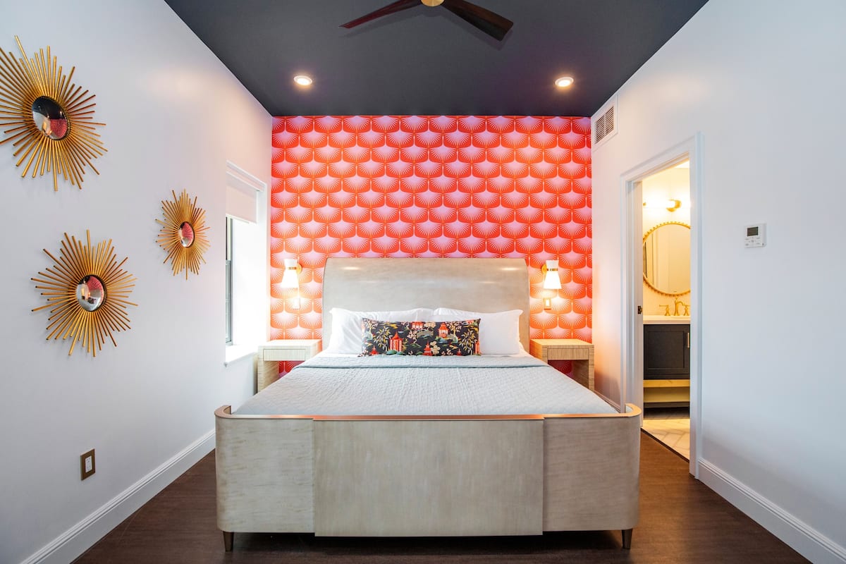 A bedroom with a bed, a ceiling fan, and a wall with a patterned wallpaper.