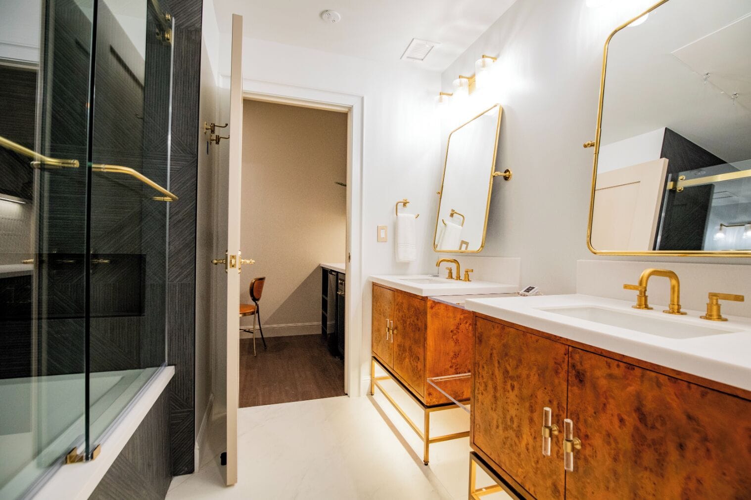 Ein modernes Badezimmer mit Duschkabine aus Glas, einem Holzbadezimmer-Möbelstück mit goldenen Armaturen und einem großen Spiegel.