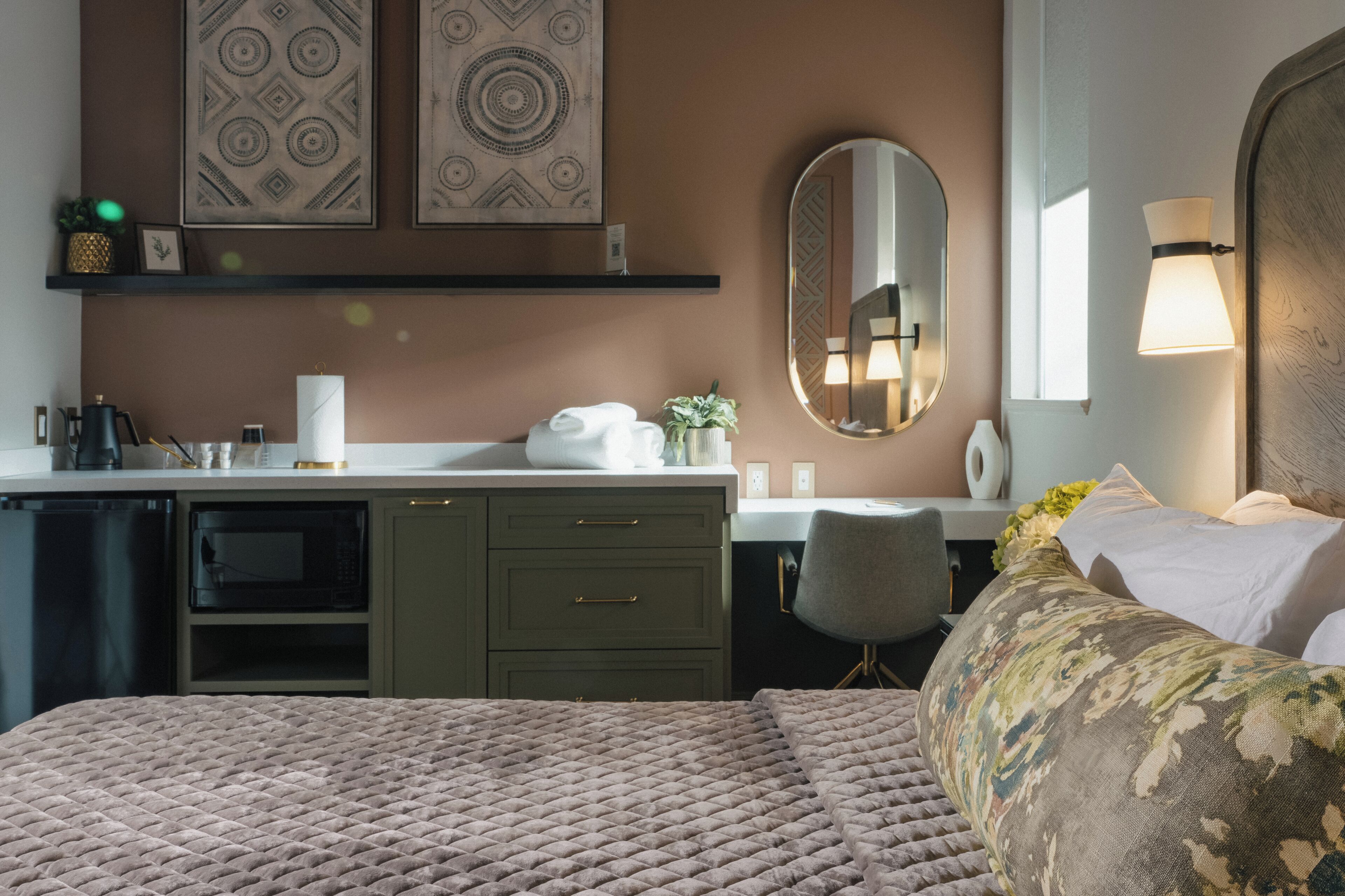 A hotel room with a bed, a desk with a chair, a microwave, a coffee maker, and a mirror.